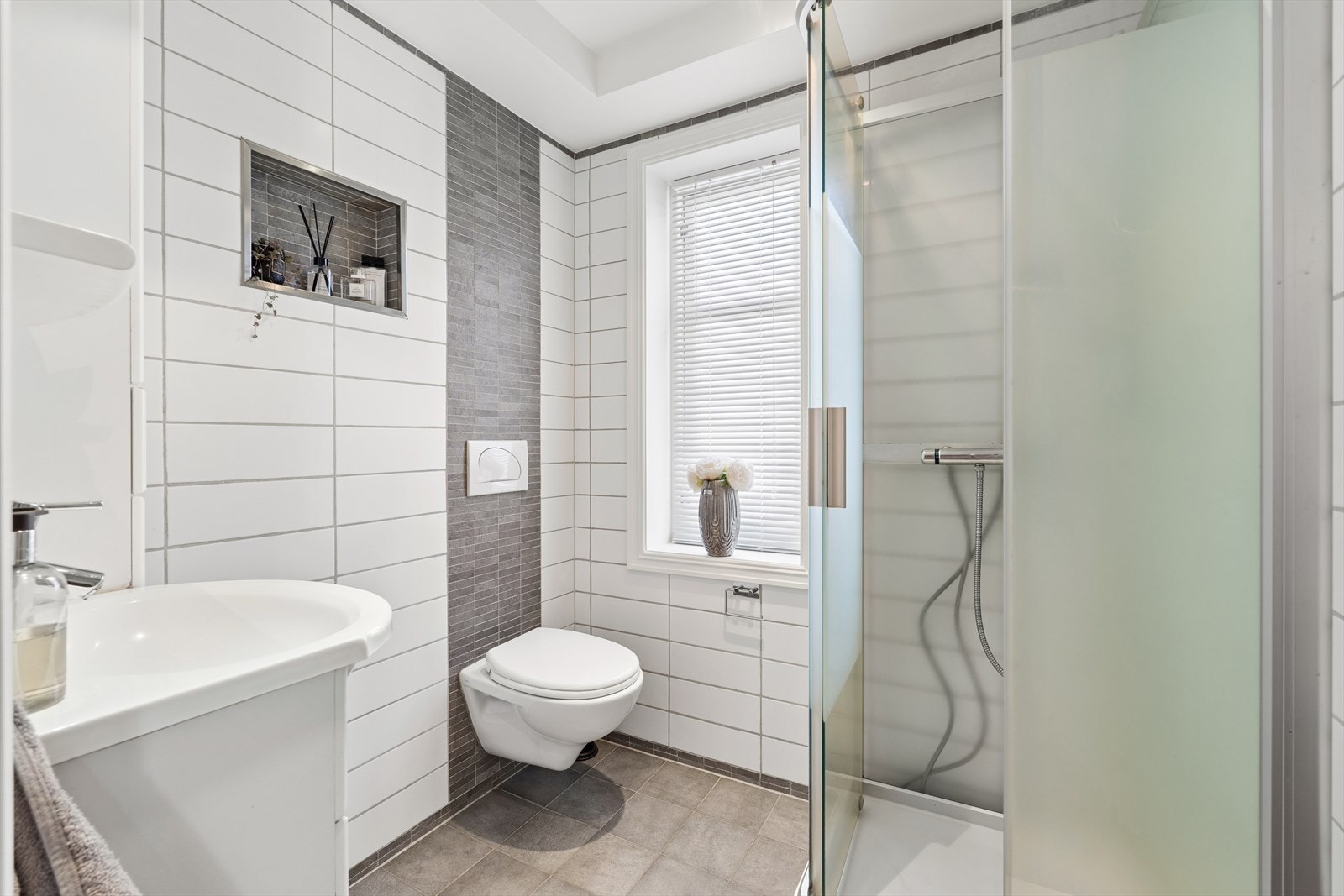 Badet i 1. etasje har keramiske fliser på vegg og flislagt gulv. Rommet har innredning med nedfelt servant, veggmontert toalett og dusjkabinett. Galleribilde