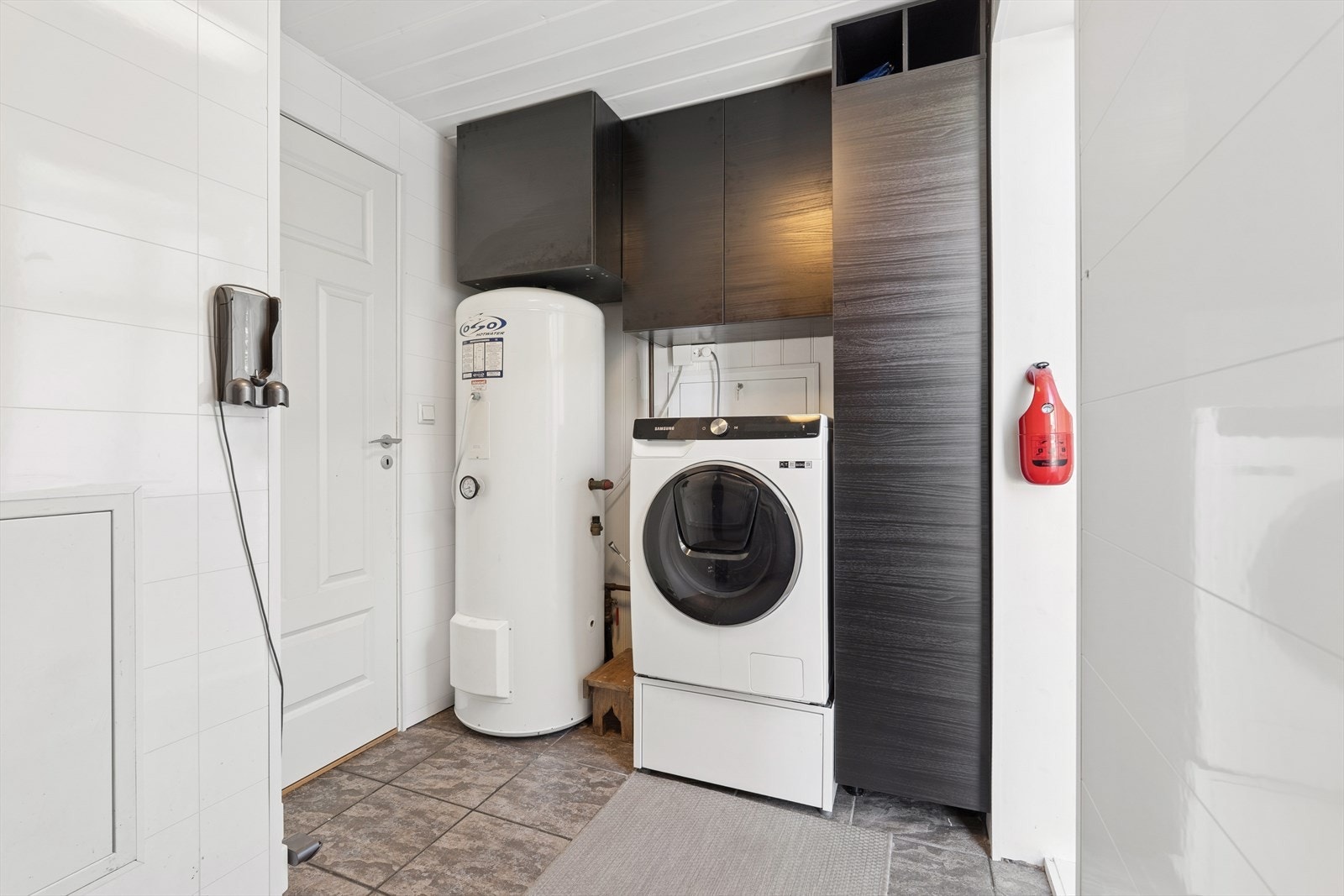 Vegg i vegg med badet i 1. etasje er det vaskerom, her er det baderomsplater på vegg og flislagt gulv. Rommet er innredet med opplegg for vaskemaskin og skapløsning. Herfra er det direkte adkomst til hagen. Galleribilde