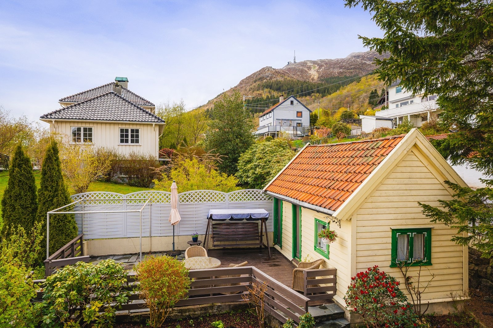 Overblikksbilde av uthus med tilhørende terrasse og fine utearealer rundt boligen. Galleribilde