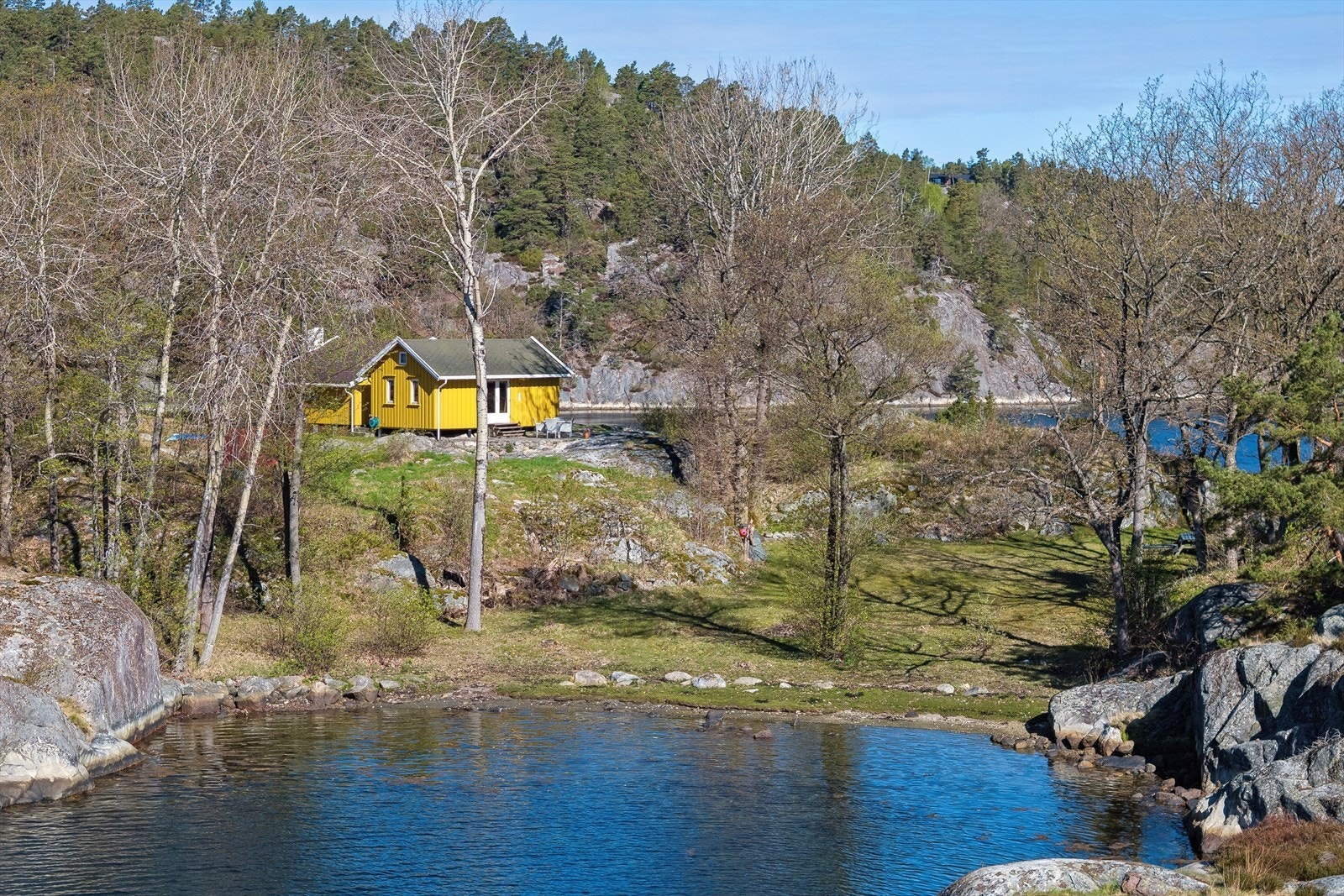 Hytta er plassert naturlig i terrenget, omgitt av svaberg og skog. Galleribilde