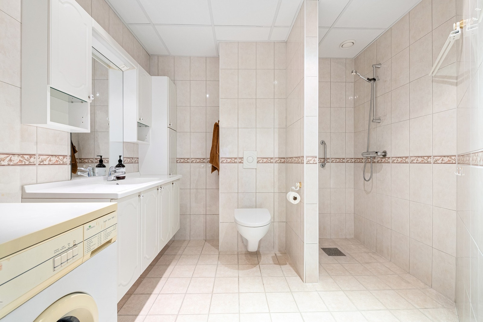 Badet har dusjnisje, vegghengt toalett og praktisk baderomsinnredning med oppbevaring Galleribilde