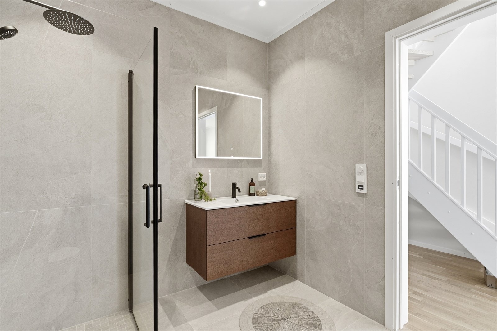Baderommet er en moderne og rolig oase med en elegant kombinasjon av store matte grå fliser som gir et tidløst uttrykk og en sofistikert følelse. Varmt naturtre og stilige sorte detaljer. Galleribilde