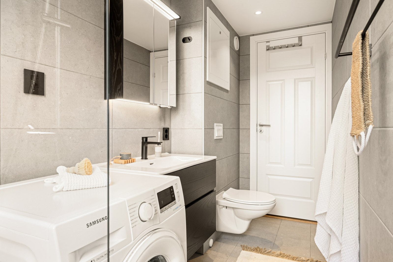 Badet er innredet med vegghengt toalett, baderomsinnredning med servant, speilskap, dusjhjørne og opplegg for vaskemaskin. Galleribilde