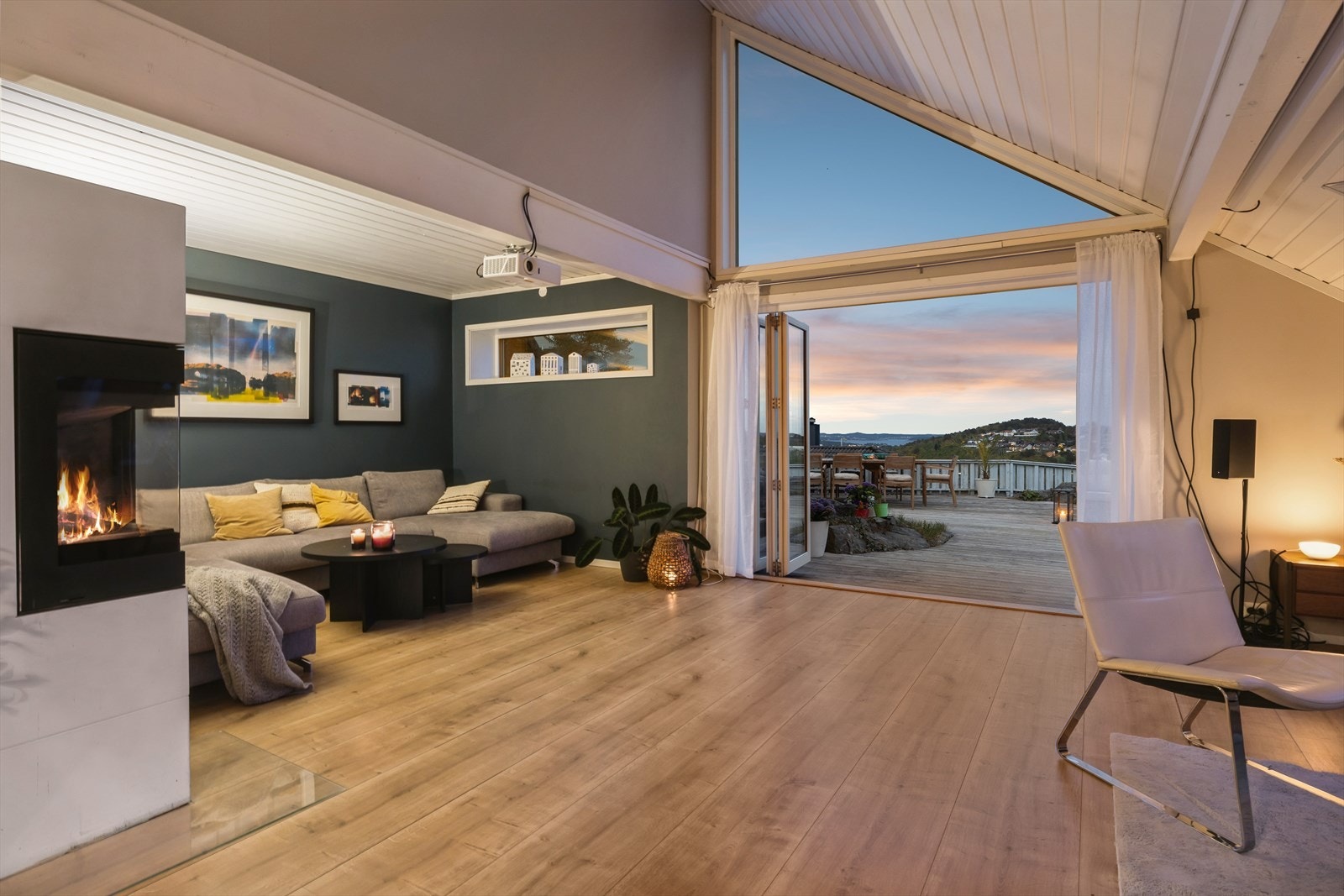 Lys og romslig stue med peis og store glassflater som åpner opp mot terrasse og utsikt - en perfekt kombinasjon av inne- og uteliv. Galleribilde