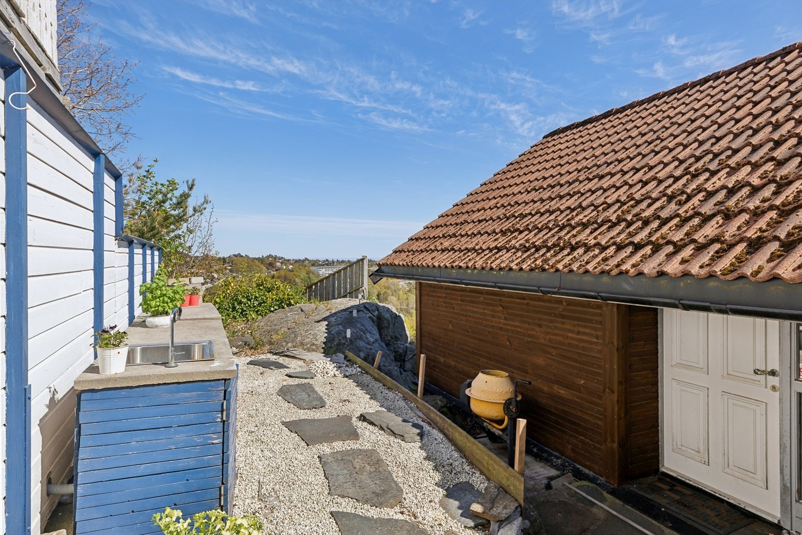 På baksiden av boligen går det en steinlagt sti som leder til hjørnet av tomten, hvor du finner et utekjøkken og opparbeidet terrasse. Galleribilde