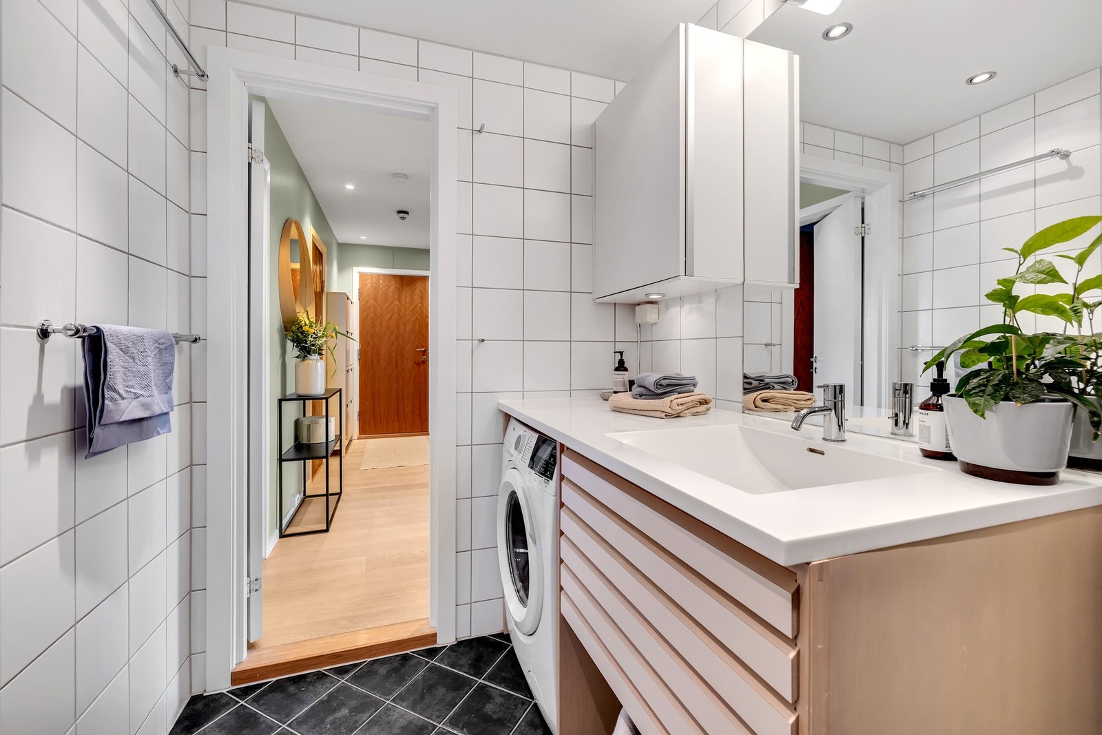 Badet er innredet med nedfelt servant, vegghengt toalett, dusjhjørne med glassvegger og opplegg for vaskemaskin. Galleribilde