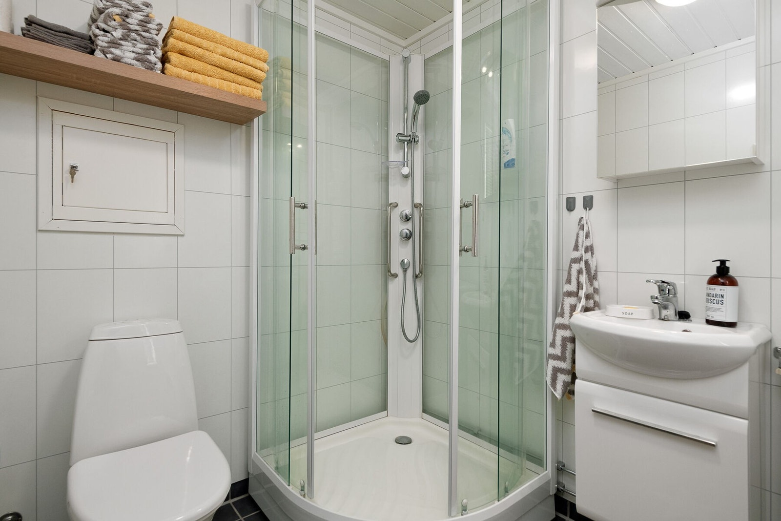 Badet er utstyrt med fliser på gulv og vegger, servant, toalett og dusjkabinett. Galleribilde