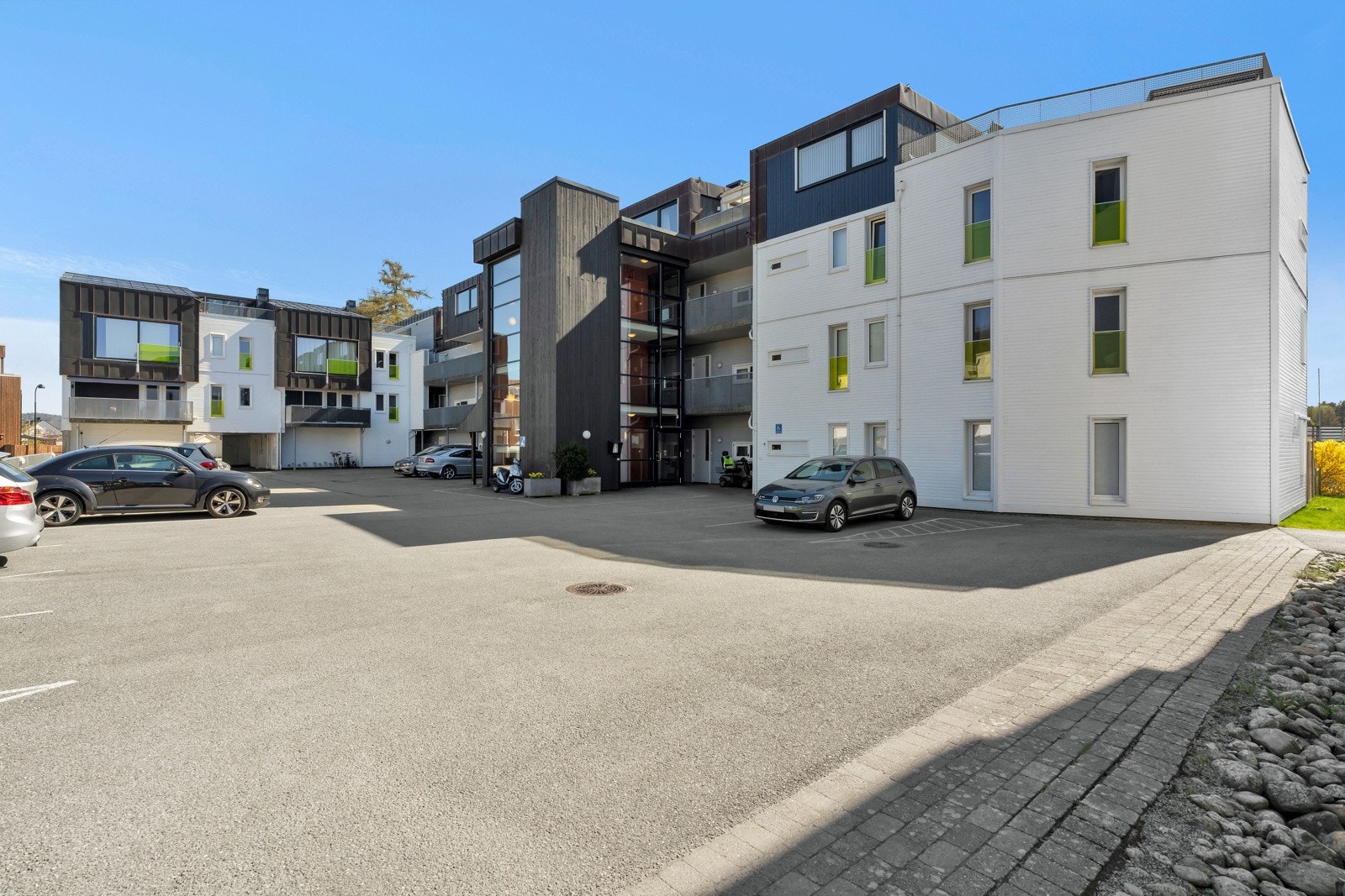 Leilighetsbygget har asfaltert innkjørsel med gjesteparkering og nedkjørsel til felles garasjekjeller. Galleribilde