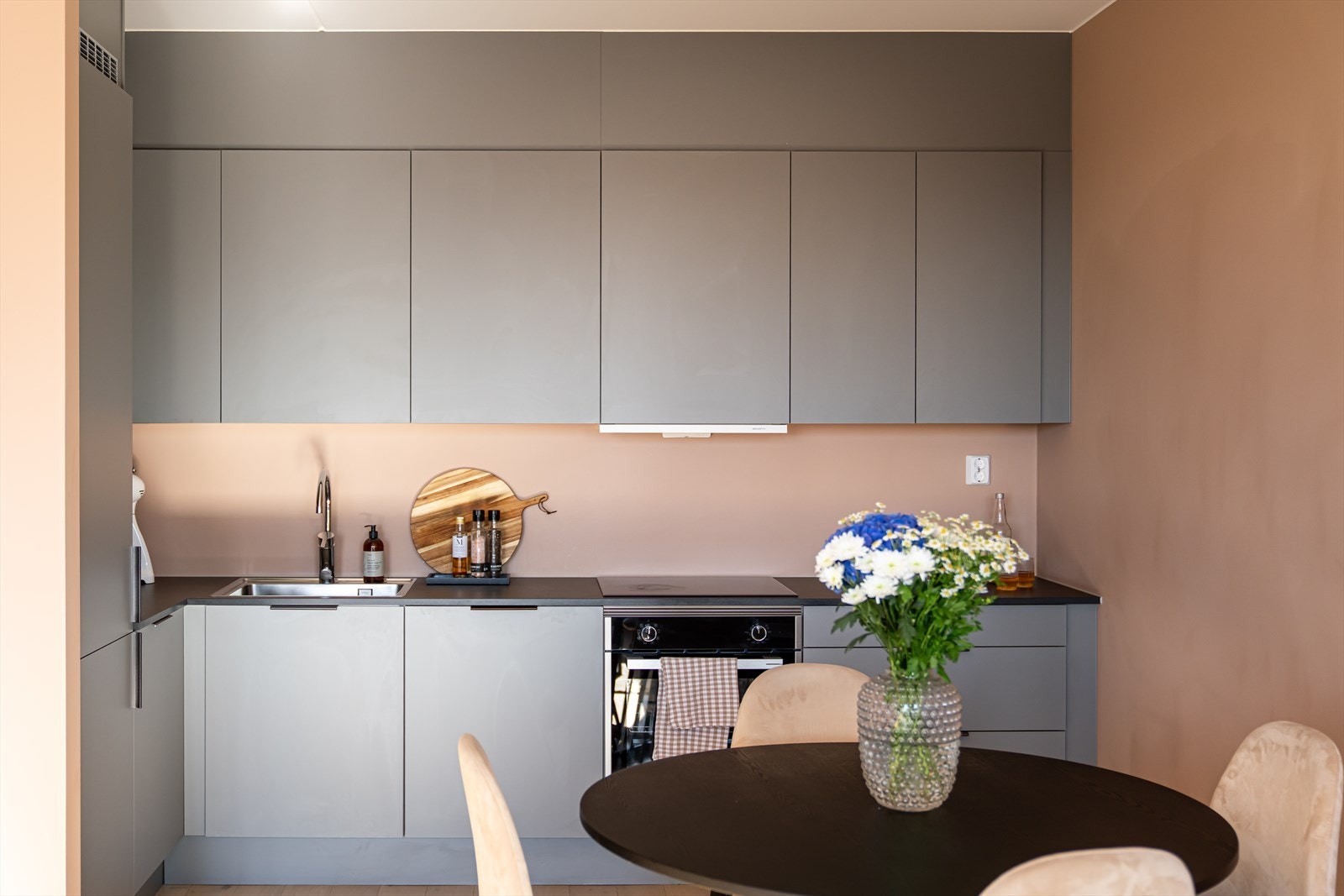 Innredningen har et moderne, men tidløst uttrykk, med grå, glatte fronter, nedfelt oppvaskkum og sort benkeplate av laminat. Galleribilde