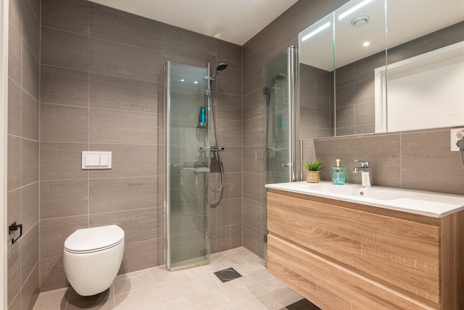 Badet er stilfullt med moderne møbler og helhetlige flisvalg. Servantskuffer og speilskap har lett tilgjengelig oppbevaringsplass. Galleribilde