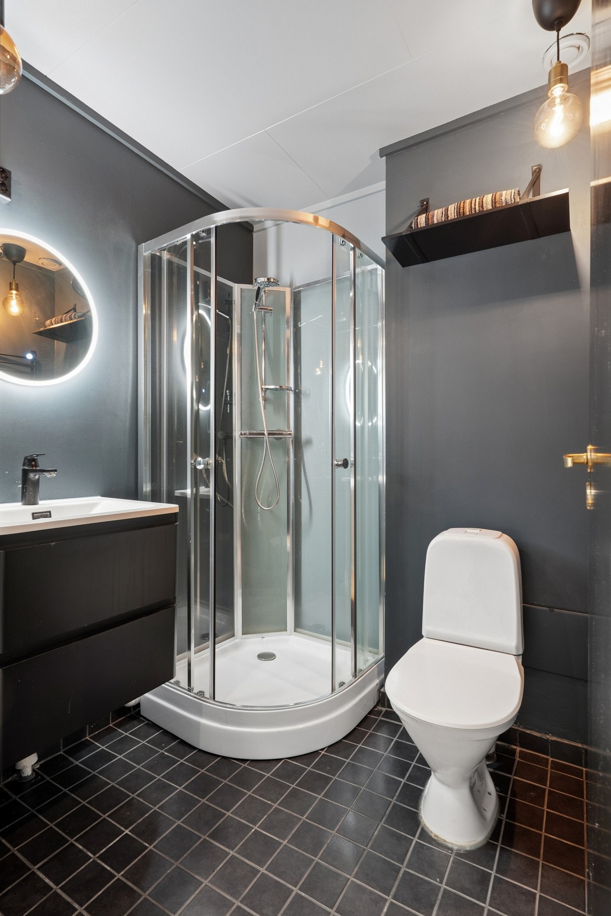 Badet har mørke gulvfliser, dusjkabinett og toalett. Galleribilde