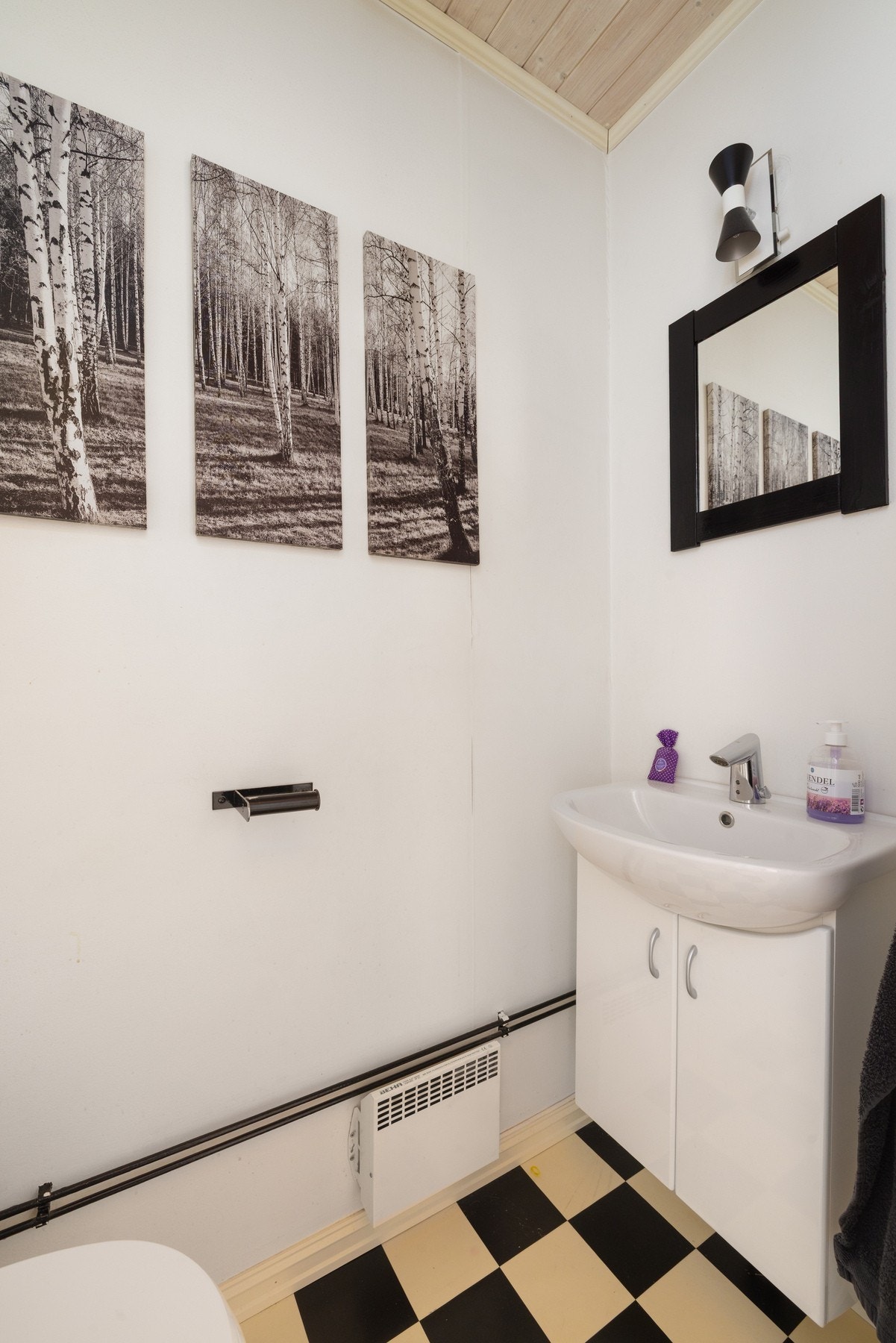 Lyst toalett med hvite vegger, sort-hvitt gulv og enkel innredning. Galleribilde