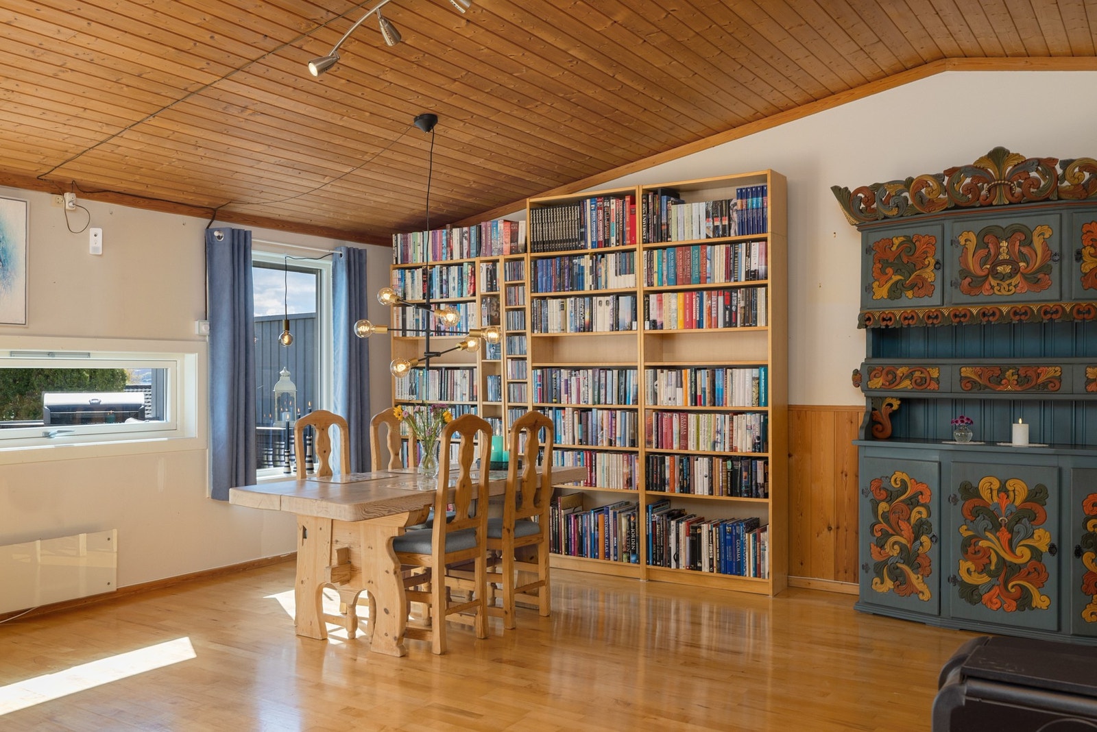 Lyst rom med tregulv og paneltak, store vinduer og bokhyller langs veggen. Galleribilde