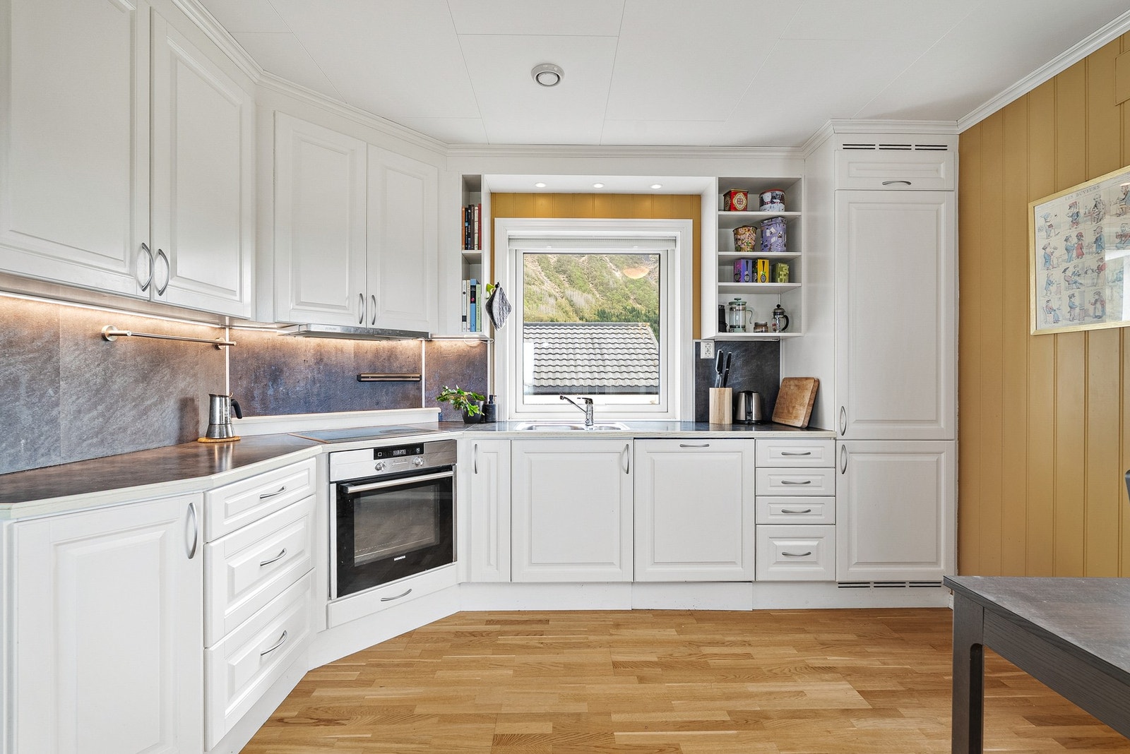 Kjøkkeninnredningen har hvite profilerte fronter, laminat benkeplate og integrerte hvitevarer. Galleribilde