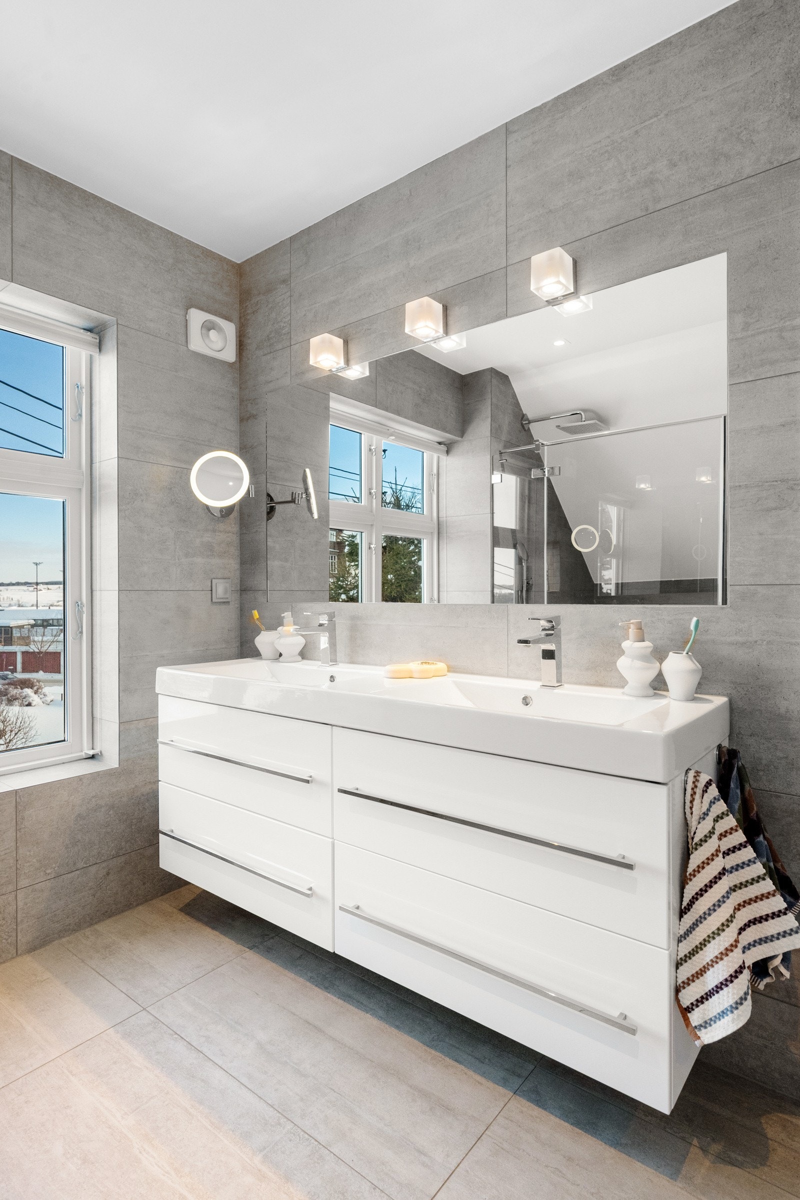 Badet har flislagte gulv- og veggflater og er innredet med dusjhjørne, badekar, vegghengt toalett og moderne baderomsinnredning. Galleribilde