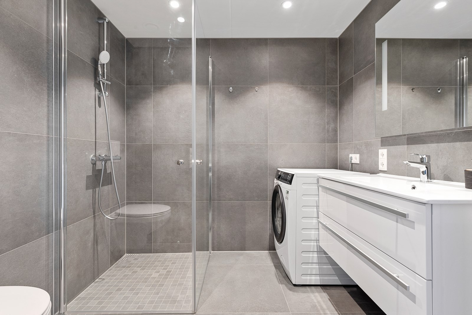 Badet er utstyrt med innfellbare dusjdører, servantskap, veggmontert wc, rørfordelingsskap, opplegg for vaskemaskin og mekanisk avtrekk. Galleribilde