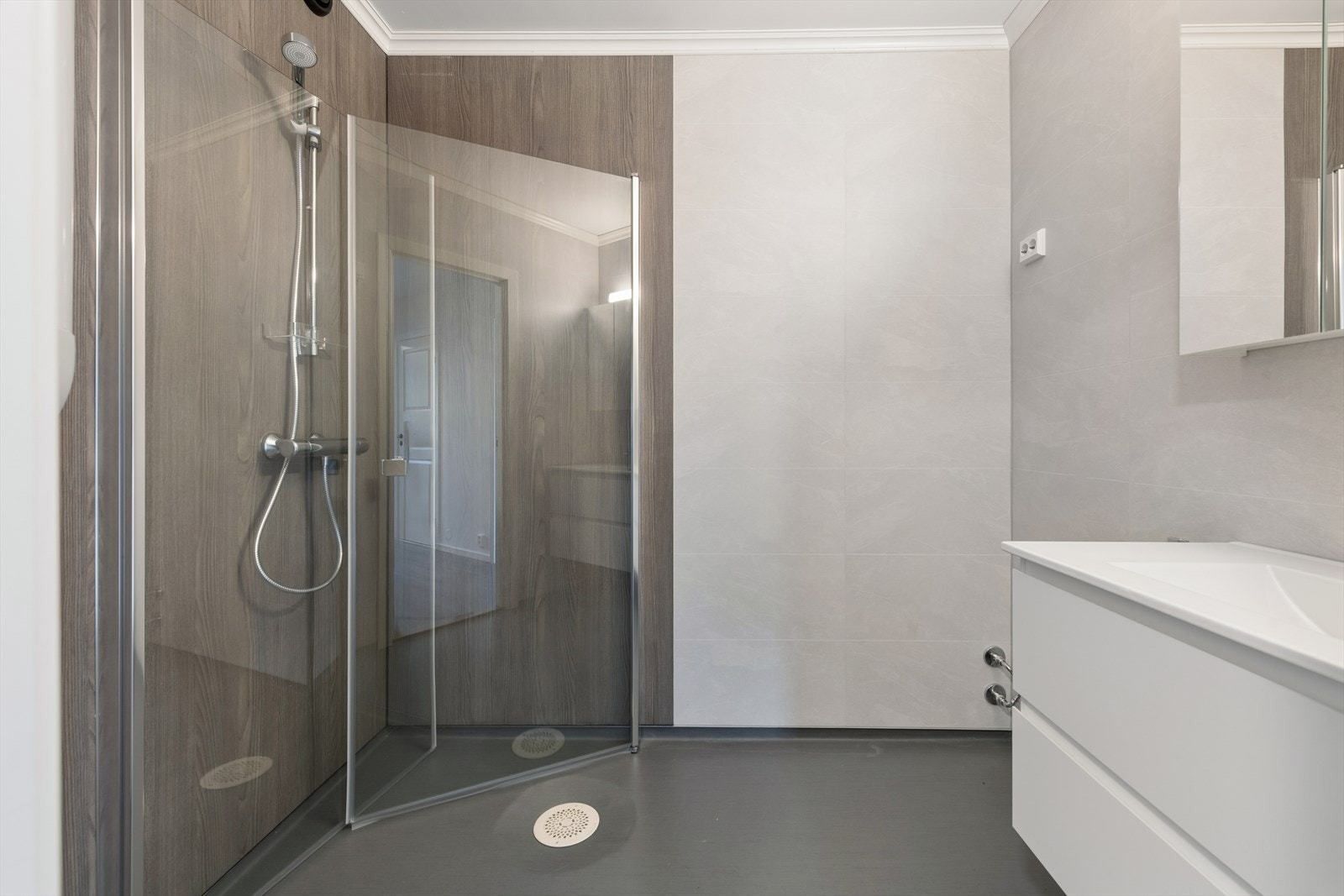 Badet er utført med våtromsbelegg på gulv, baderomspaneler på veggene og et praktisk dusjhjørne med glassdører. Galleribilde