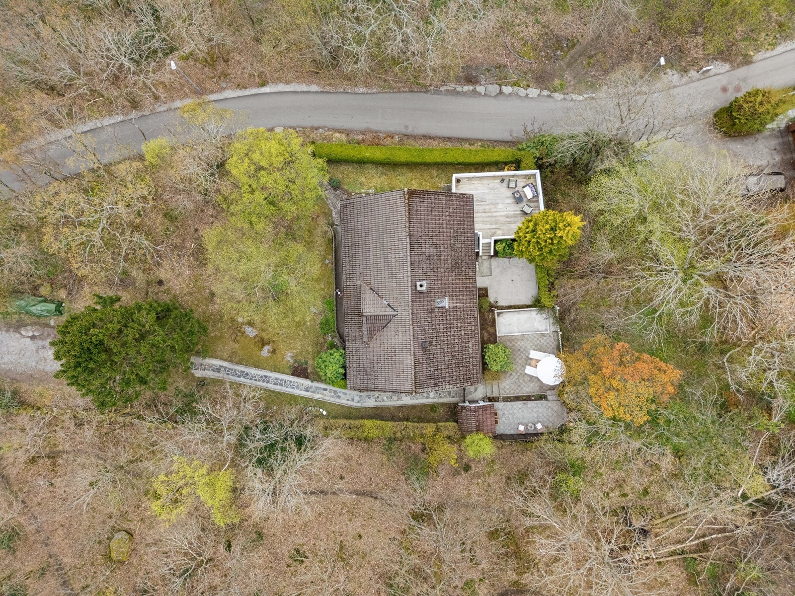 Eiendommen ligger i et skrånet terreng, omkranset av trær og grøntarealer. Galleribilde