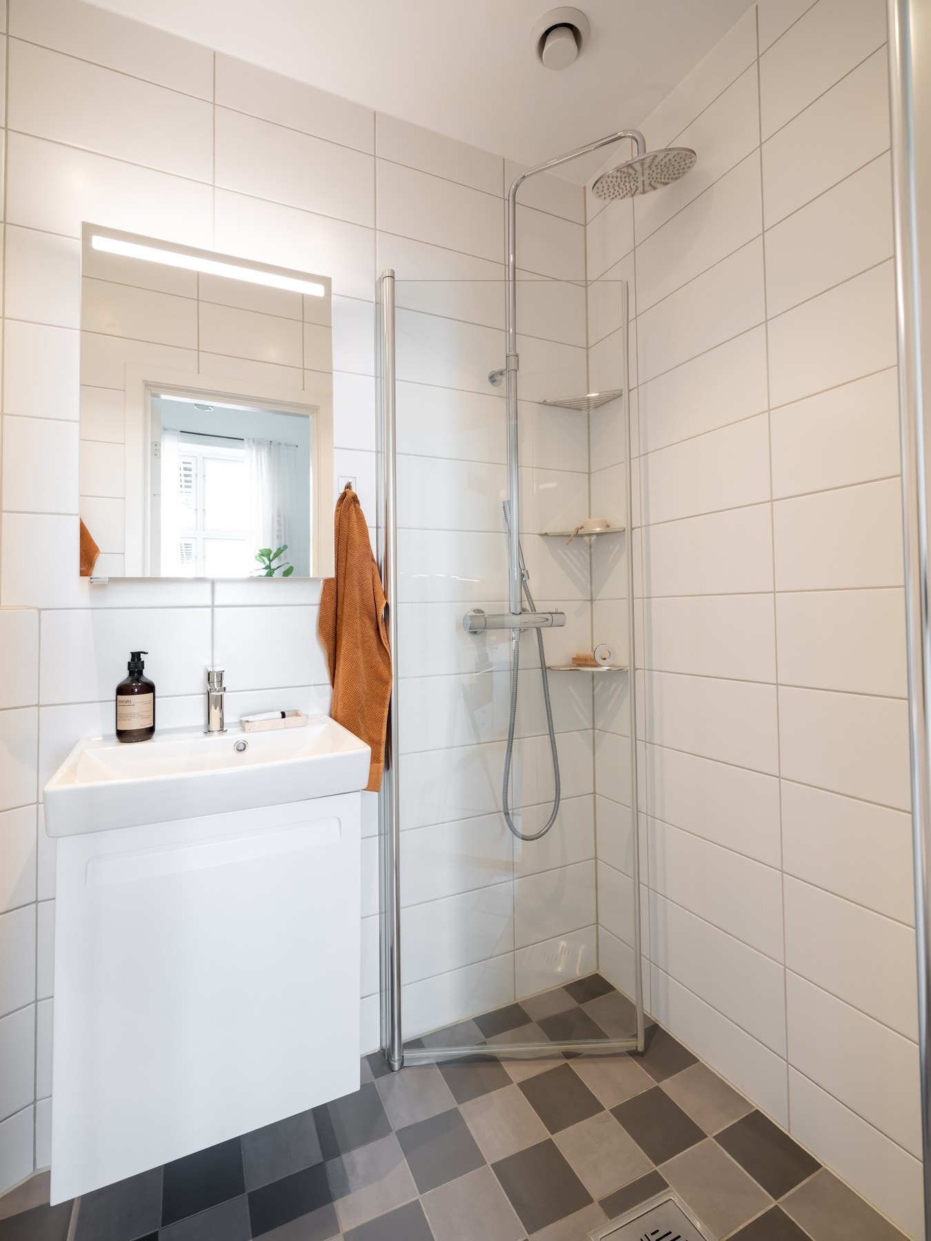 Badet er innredet med servant på underskap, speil med belysning, vegghengt toalett og dusjhjørne. Galleribilde