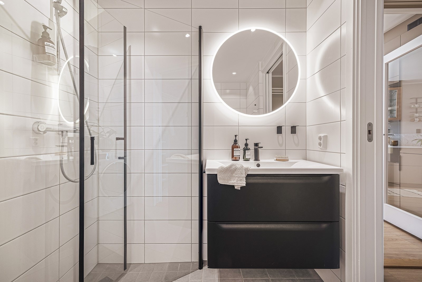 Badet er innredet med veggmontert toalett, dusjhjørne, skuffeseksjon med overliggende servant, og opplegg for vaskemaskin. Det er avtrekk til balansert ventilasjonsanlegg. Galleribilde