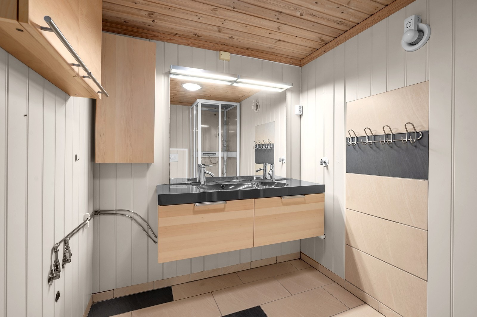 Badet har fliser på gulv, panelplater på vegg og en dobbel servantinnredning. Galleribilde