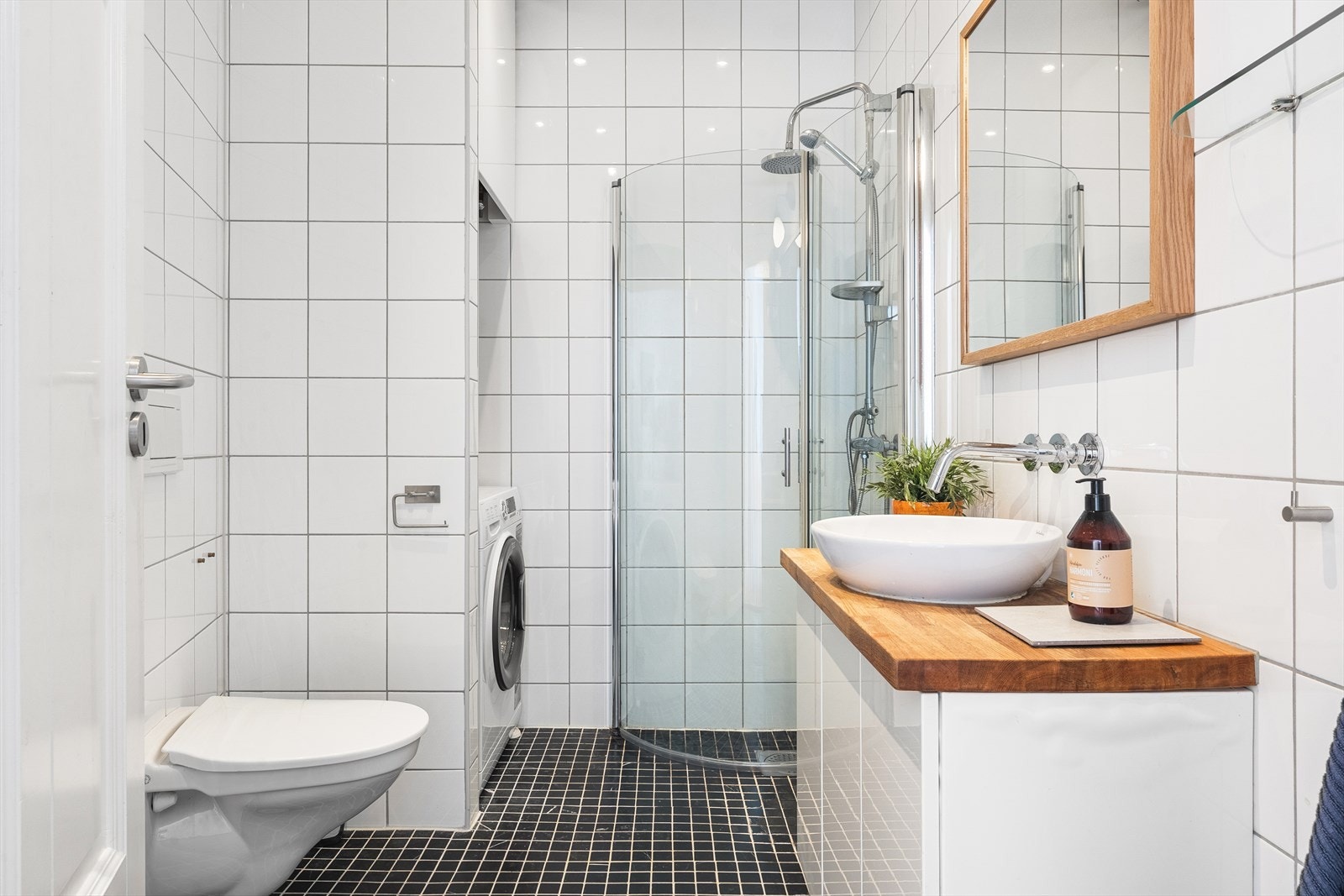 Badet inneholder baderomsinnredning med servant, vegghengt toalett, dusjvegger og opplegg for vaskemaskin Galleribilde