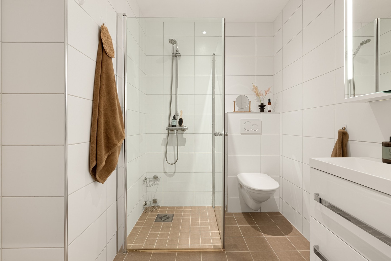 Badet har delikate overflater og er praktisk innredet med vegghengt toalett, servantmøbel med skuffer og overhengende speilskap og dusj med innfellbare glassdører. Galleribilde