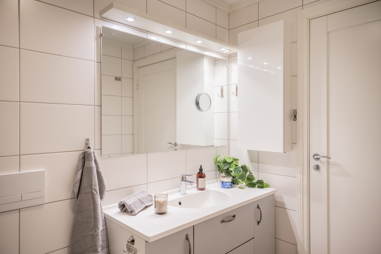 Badet er innredet med dusjvegger av glass, vegghengt toalett, servant med underskap, og opplegg for vaskemaskin og tørketrommel. Galleribilde