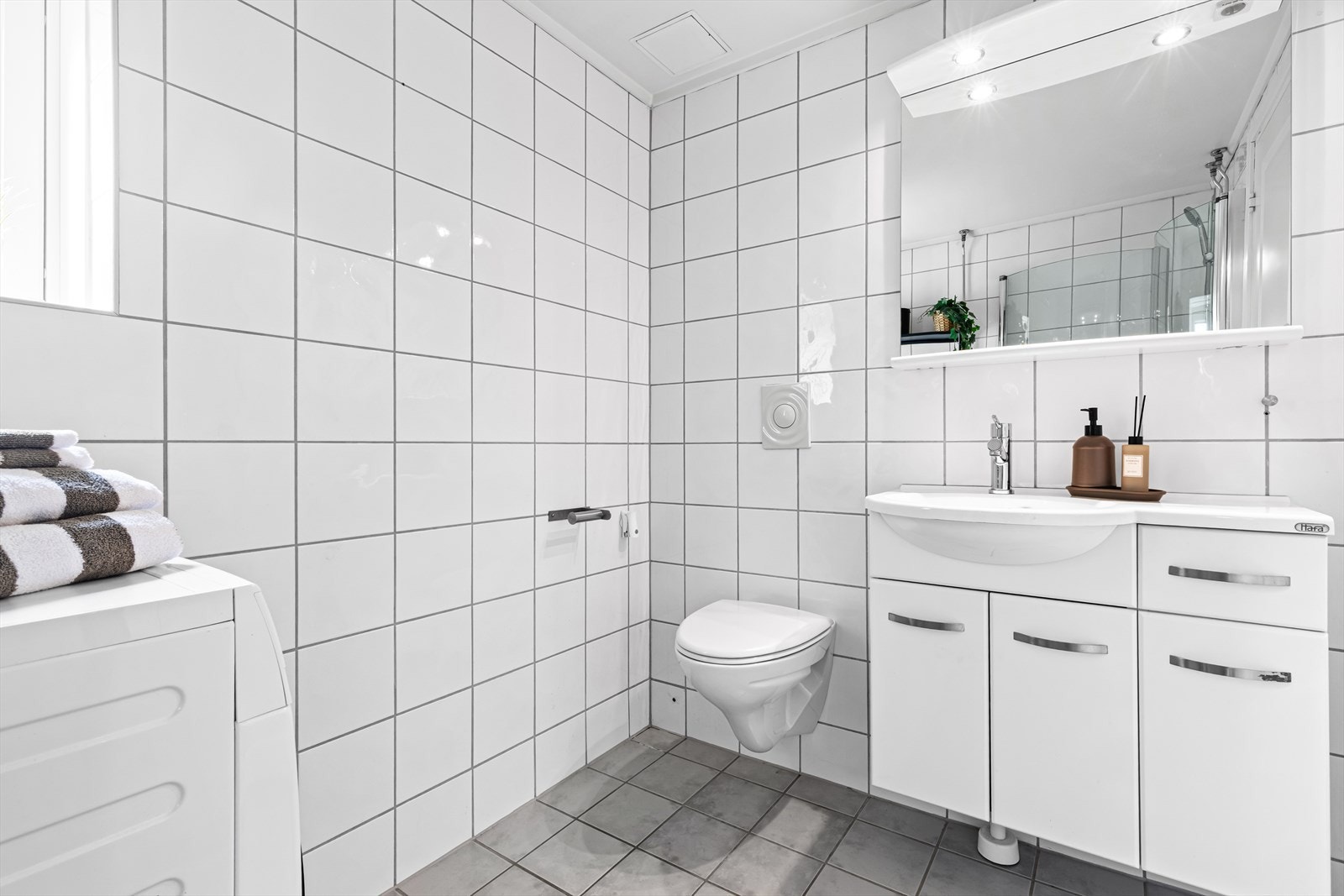 Badet er innredet med servant med underskap, speil med belysning og veggmontert toalett. Galleribilde