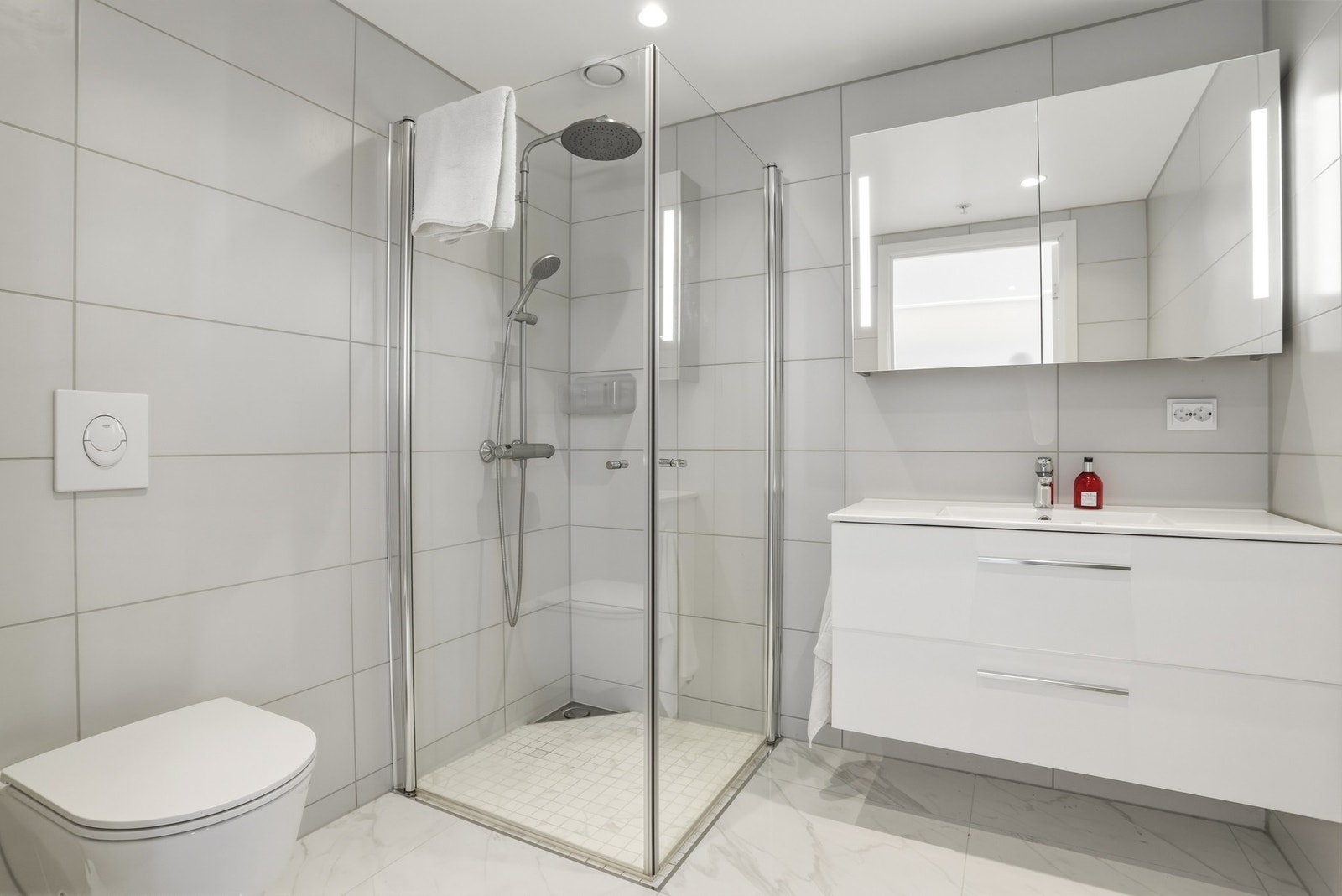 Det andre badet ligger i suiteløsning med hovedsoverommet og har hvite fliser på veggene, downlights i himlingen og store, hvite kunst fliser i marmor look på gulv med vannbåren gulvvarme. Baderomsinnredningen har hvite fronter og består av en heldekkende Galleribilde