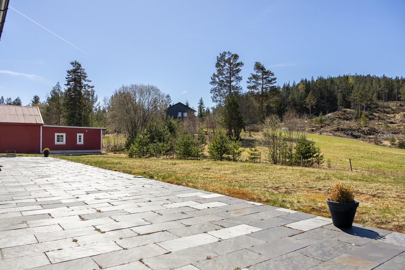 Den overbygde terrassen leder ut til en stor platting og hageområde. Galleribilde