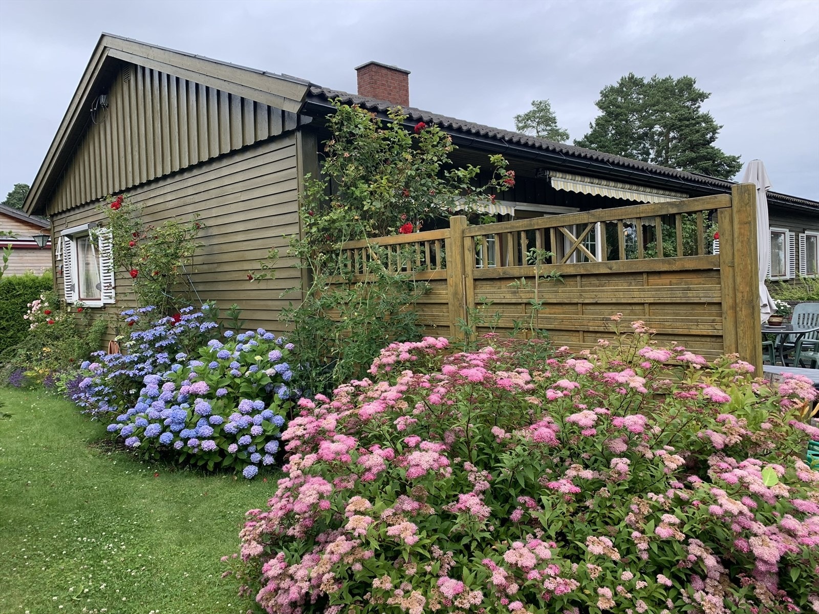 Foto tatt av selger. Hagen er pent beplantet med busker og blomster som skaper en frodig ramme rundt eiendommen. Galleribilde