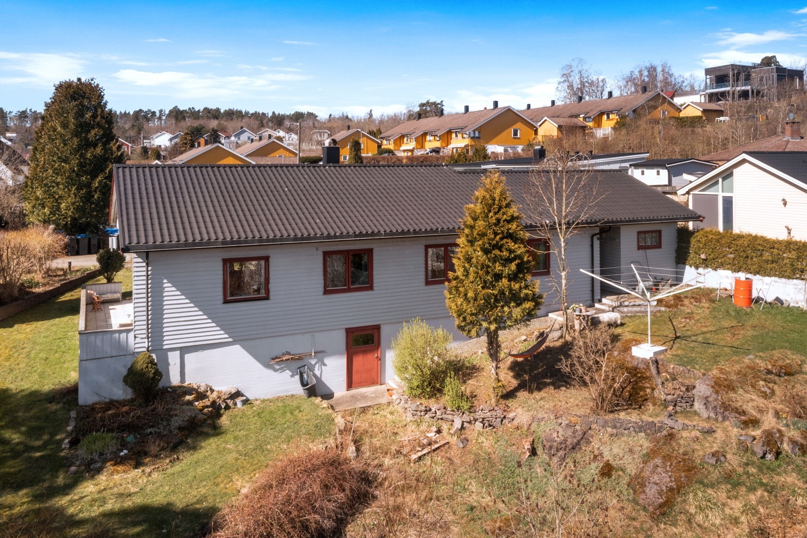 Boligen sett fra hagesiden med terrasse, grøntarealer og praktisk adkomst til kjellerrom. Galleribilde
