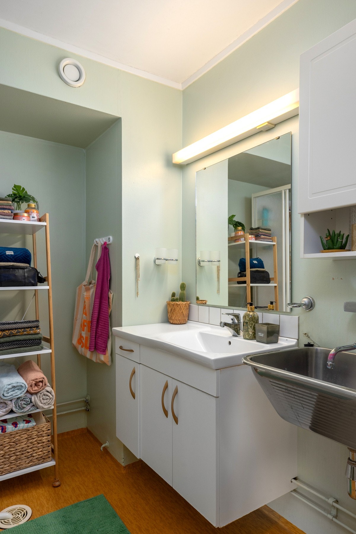 Badet har servant med underskap, speil med belysning, og en enkel vaskekum. Vegghengt hylle gir ekstra oppbevaringsplass. Galleribilde