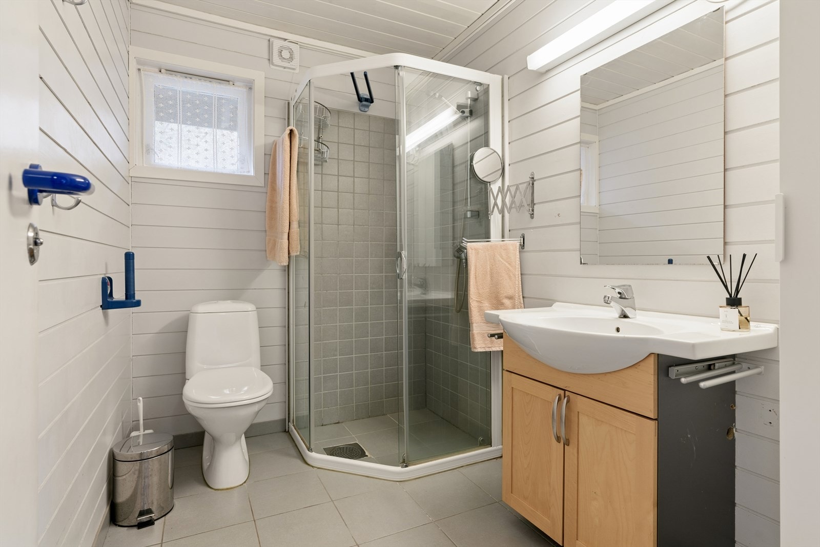 Badet med flislagt gulv og dusjnisje, med panel på øvrige vegger. Rommet er innredet med gulvmontert toalett, servant og har en elektrisk styrt vifte. Galleribilde