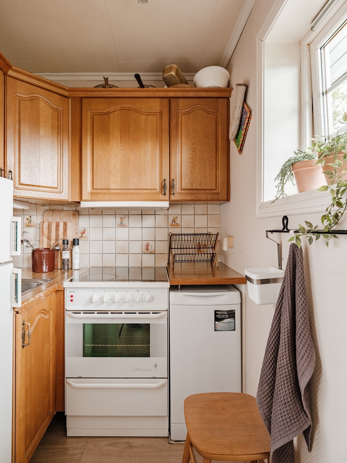 Kjøkkeninnredning med profilerte fronter, fliser på vegg over benkeskap og laminat benkeplate. Kjøkkenet er innredet med kjøleskap og komfyr. Det er kjøkkenventilator med avtrekk ut. Galleribilde