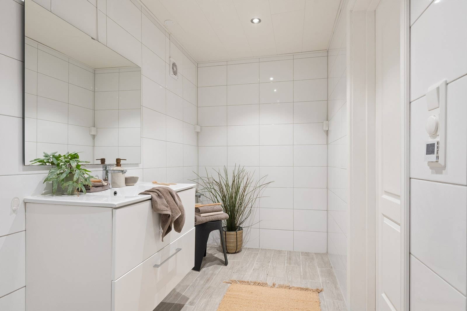 Badet er utstyrt med gulvstående toalett, dusjhjørne og servantinnredning med skuffer. Speil er montert over servanten. Galleribilde