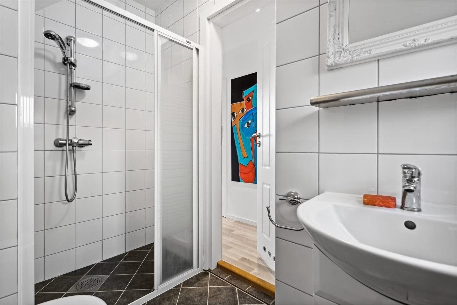 Badet er innredet med vegghengt toalett, vask med underskap, speil og dusj med skyvedører. Galleribilde