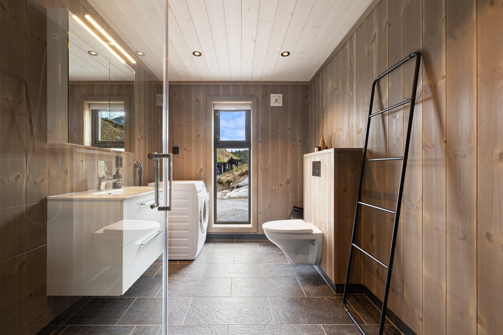 Badet har en lun og gjennomført utførelse med kombinasjon av fliser og panel/tømmer på veggene, som gir et helhetlig uttrykk tilpasset hyttens stil. Det er også opplegg for vaskemaskin. Galleribilde