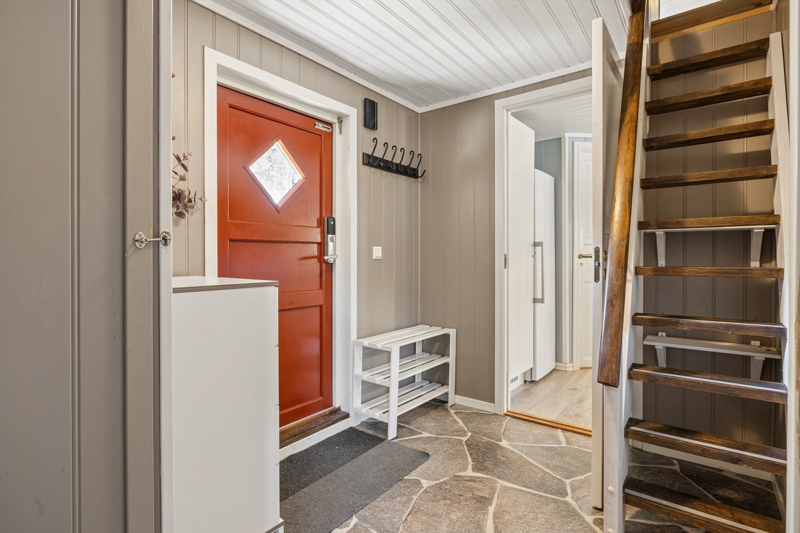 Entréen ønsker velkommen med et solid steinbelegg. Herfra er det tilgang til bad og soverom, samt en trappestige opp til hems/loft. Galleribilde
