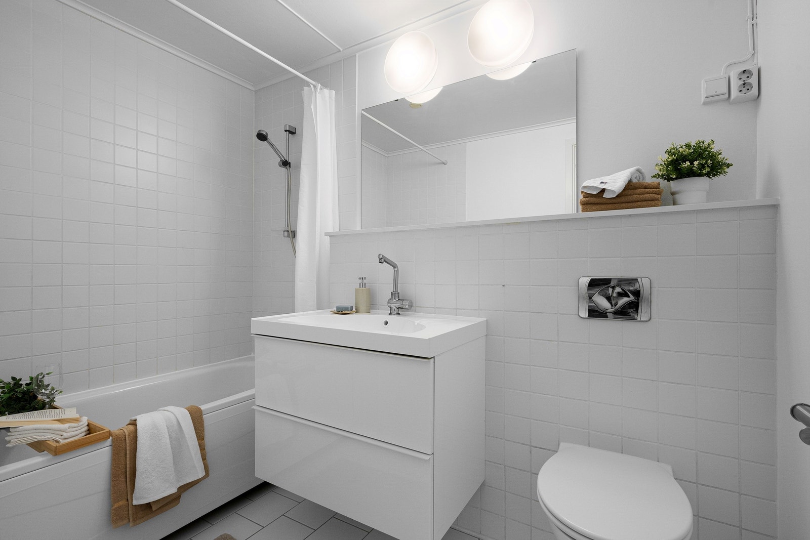 Bad I med fliser på gulv og delvis på vegg, varme i gulv.
Det er vegghengt toalett, badekar med dusj, servant med skuffer . Galleribilde