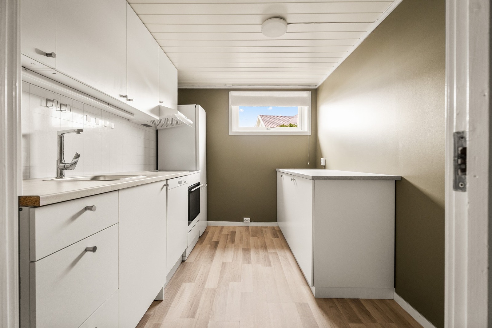 Kjøkkeninnredningen ble utvidet med flere skap i 2025. Her er det hvite, glatte fronter, benkeplate av laminat og nedfelt oppvaskkum i stål. Galleribilde