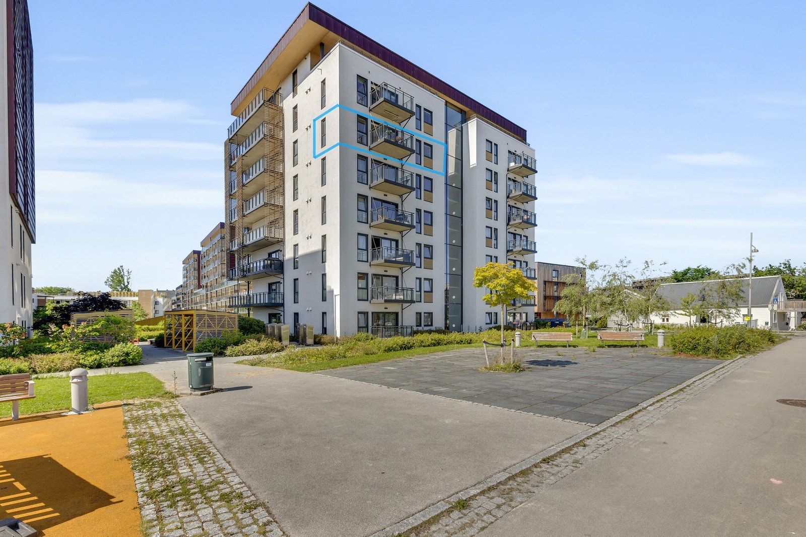 Fasadebilde. Rundt og mellom blokkene er det et pent og opparbeidet uteområde som på sommerhalvåret oppleves grønt og frodig. Leilighetens beliggenhet er markert med blå ramme. Galleribilde