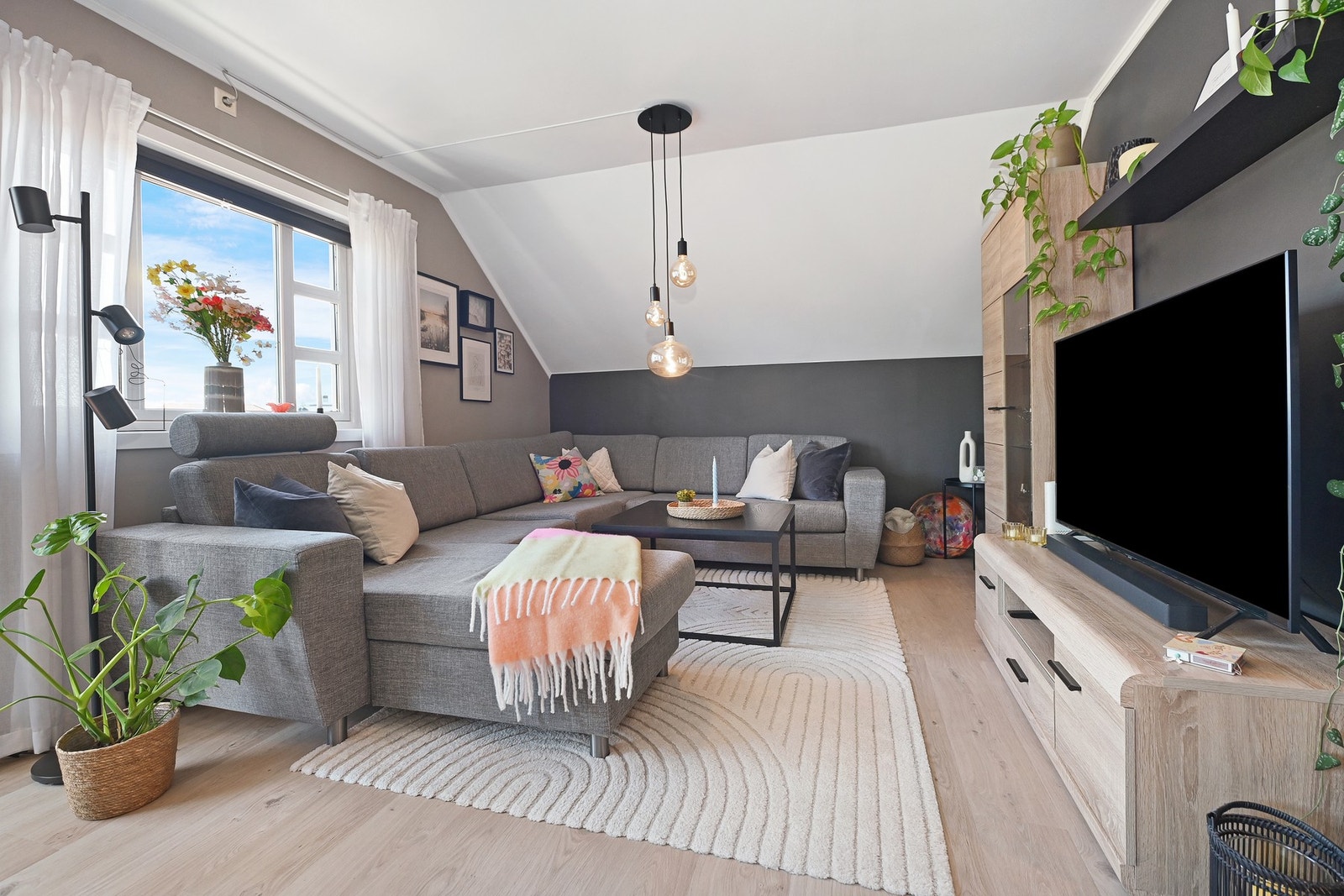 Romslig stue med store vinduer og skråtak, moderne belysning og lyse gulv. Galleribilde