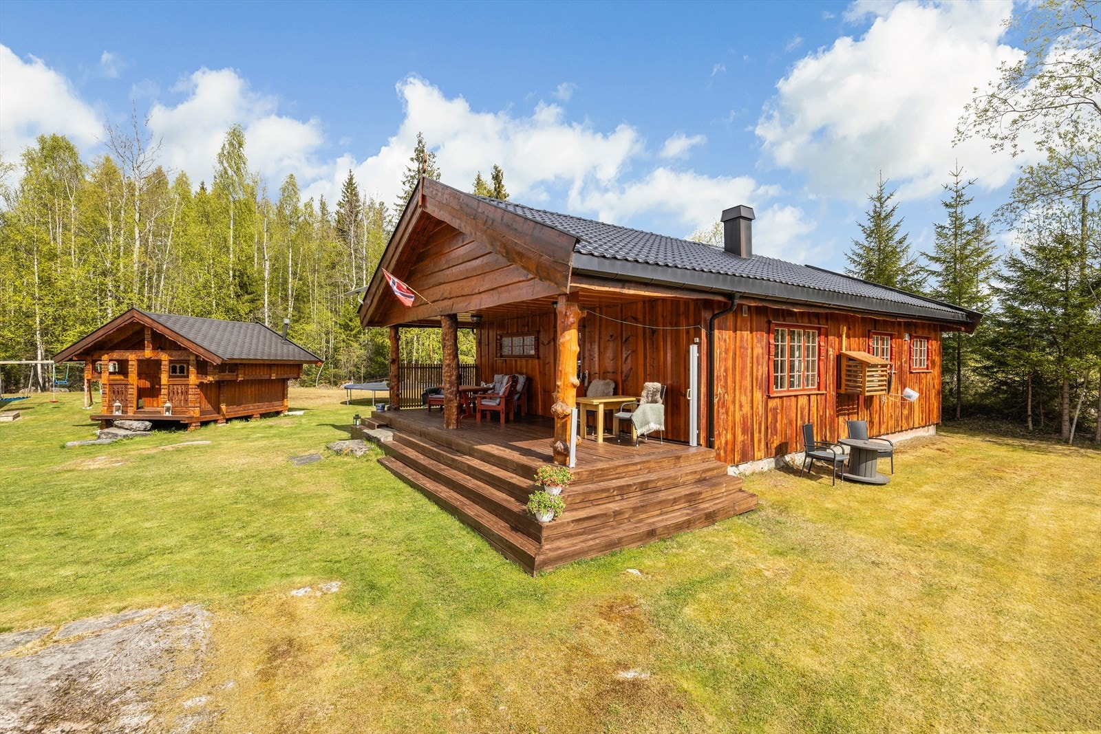 Hovedhytta og stabburet sett fra tunet. Ytterveggene er kledd med villmarkspanel. Galleribilde