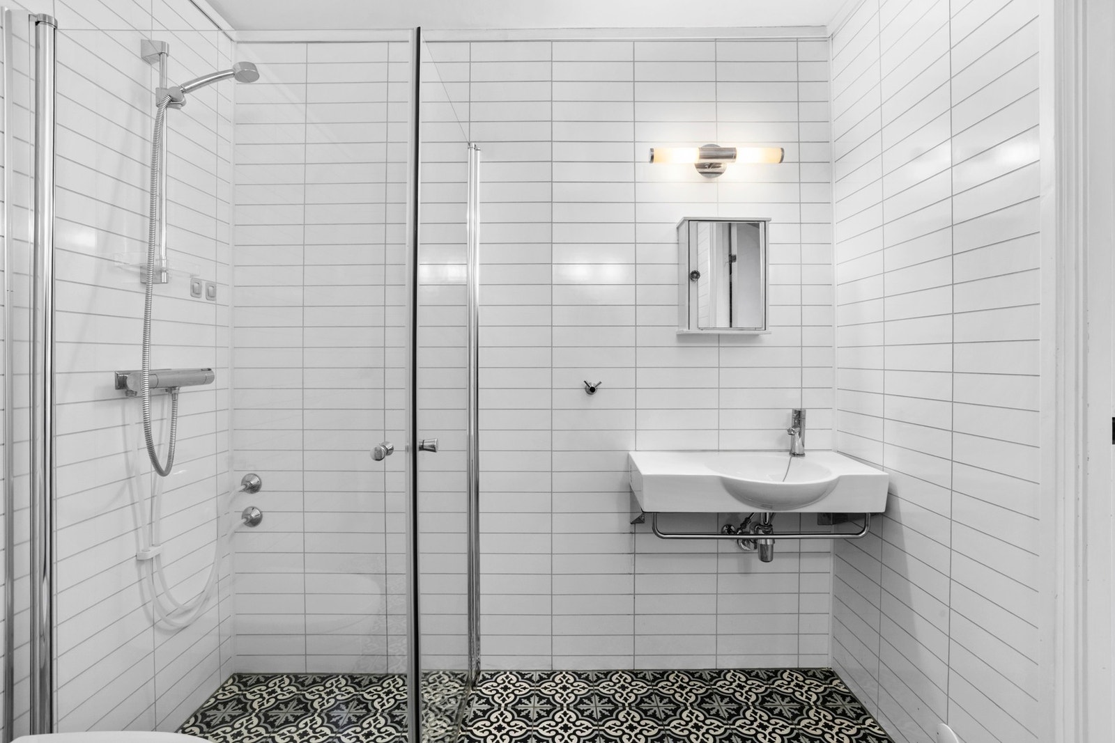 Badet er utstyrt med vegghengt servant med armatur, speilskap med overlys, vegghengt baderomsmøbel, dusjhjørne med glassdører og gulvstående toalett Galleribilde
