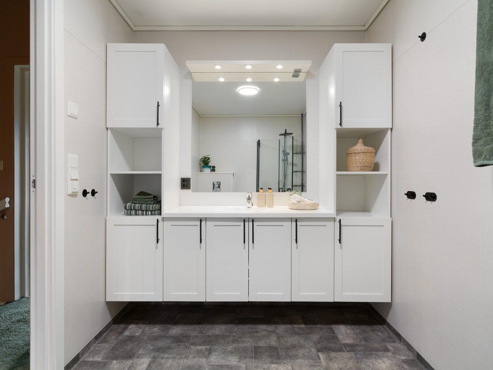 Badet har vinylbelegg på både gulv og vegger. Badet er innredet med servantskap, veggskap og speil. Videre er rommet utstyrt med toalett og innfellbare dusjvegger. Galleribilde