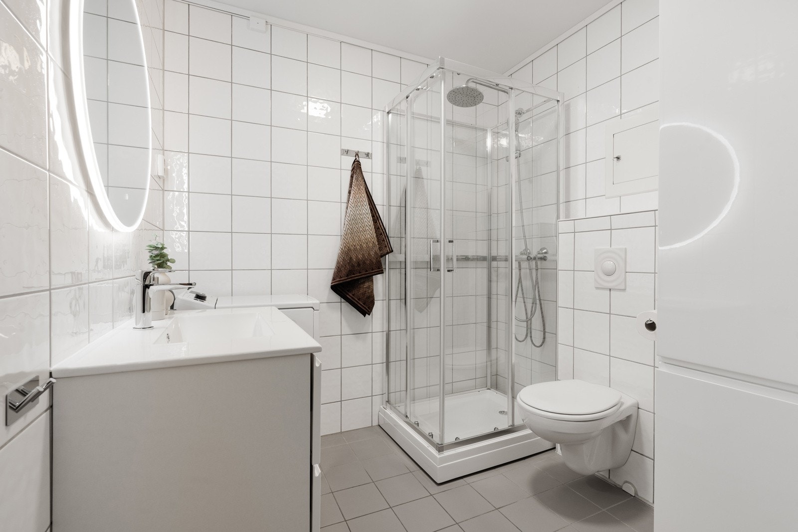 Flislagt bad med gulvvarme, wc, dusjkabinett, baderomsinnredning og opplegg for vaskemaskin. Galleribilde