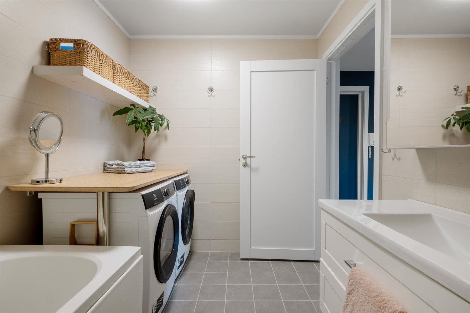 Stilrent og flislagt bad med varmekabler. Innredet med servant med underskap, speil, badekar med dusj, opplegg for vaskemaskin og tørketrommel med benkeplate over. Galleribilde