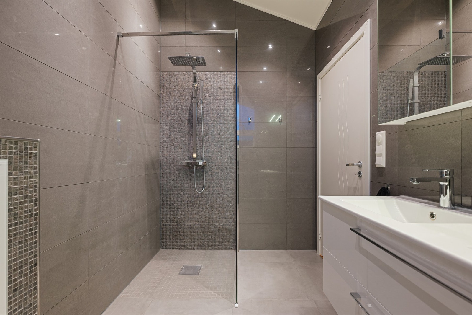 Badet i loftsetasjen fremstår moderne og delikat med flislagte overflater og en stilren innredning. Galleribilde